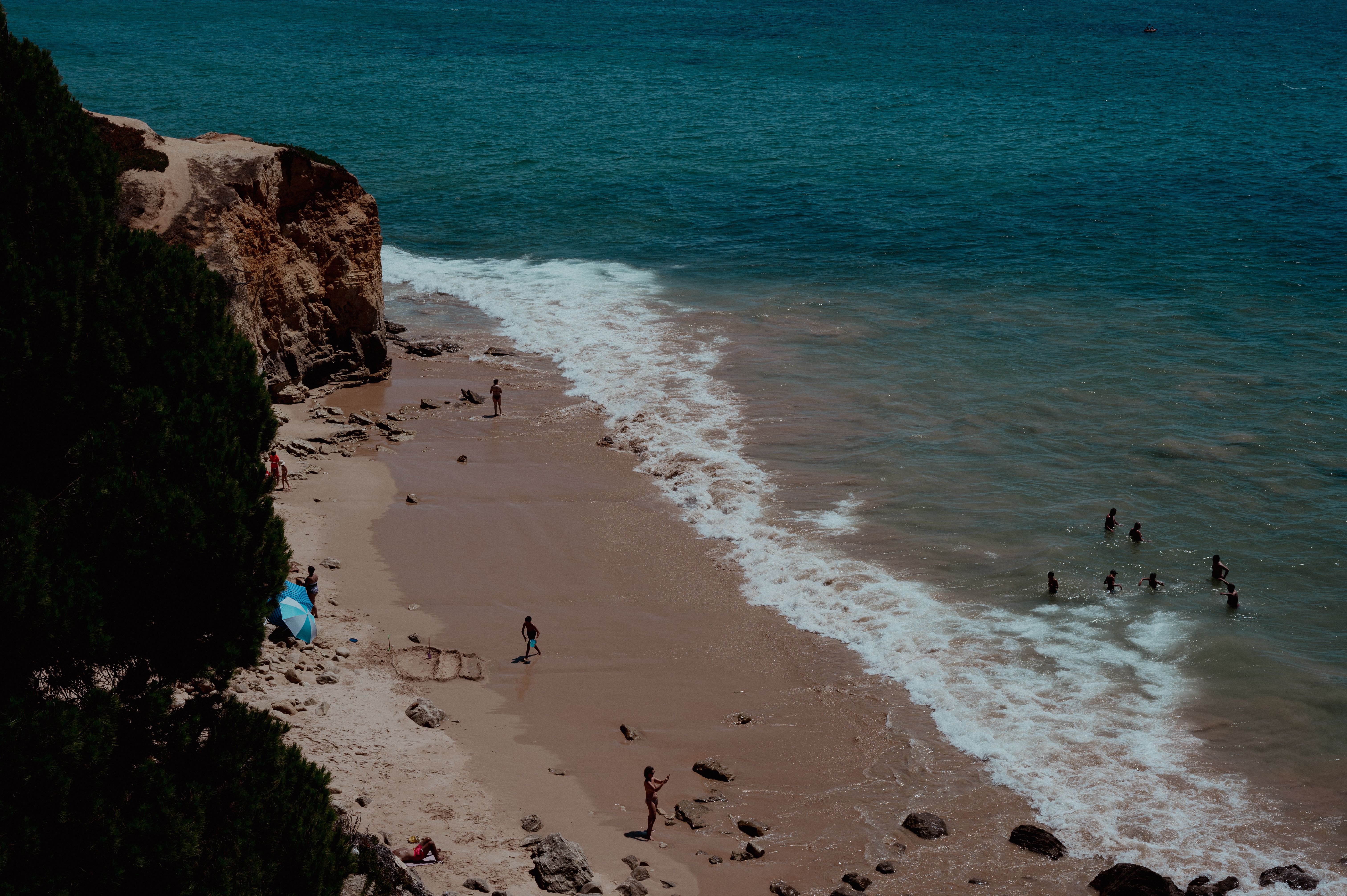 Aerial view of a tranquil beach with people enjoying the ocean and cliffs in a vibrant summer setting.