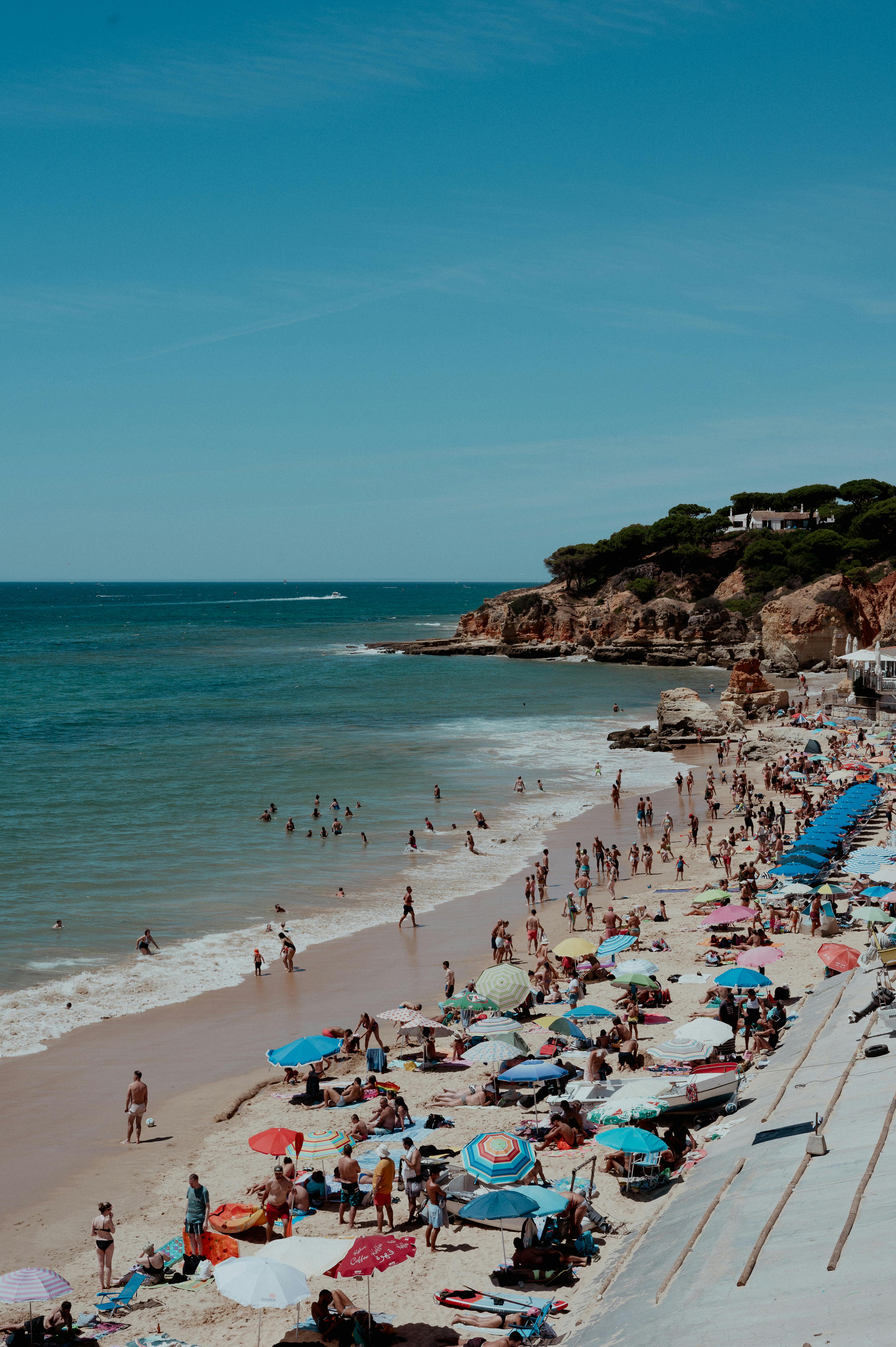 Crowded beach scene with sunbathers and swimmers under a clear sky.