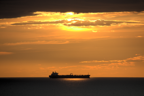 Free A cargo ship silhouetted against a stunning golden sunset on the open sea. Stock Photo