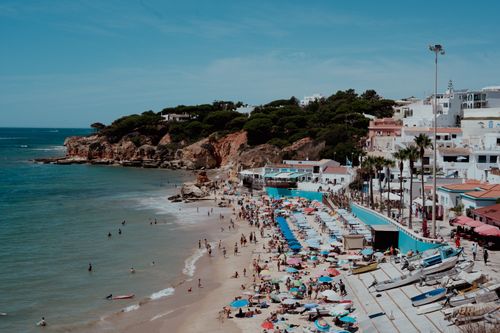 Free Vibrant beach scene with sunbathers, umbrellas, and cliffside buildings. Stock Photo