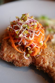 Delicious crispy breaded pork chop topped with fresh carrots and sprouts, perfect for a gourmet meal.