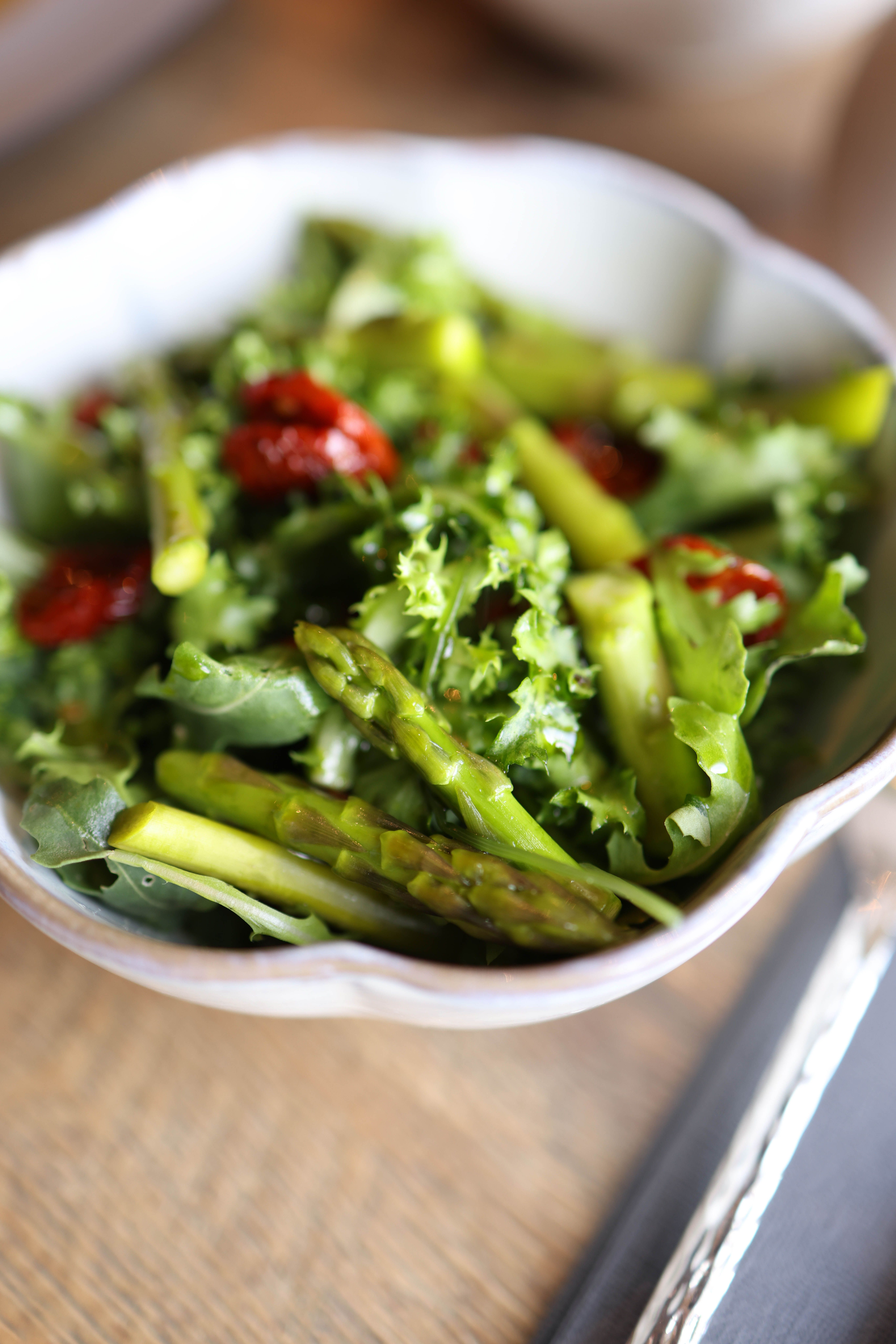 Close-up of a fresh green salad with asparagus and sun-dried tomatoes in a white bowl.
