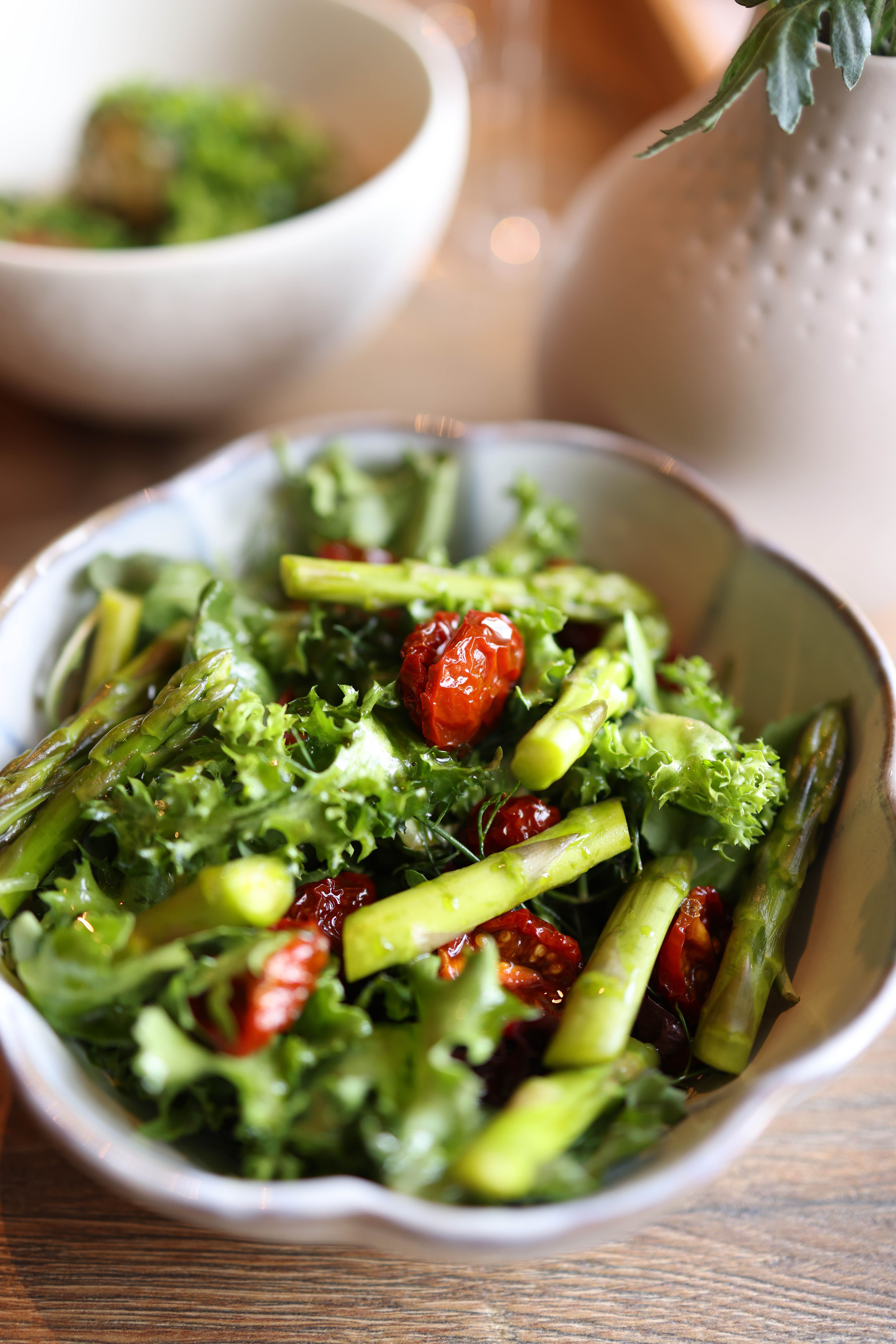 Close-up of fresh salad with asparagus, cherry tomatoes, and mixed greens in a ceramic bowl.
