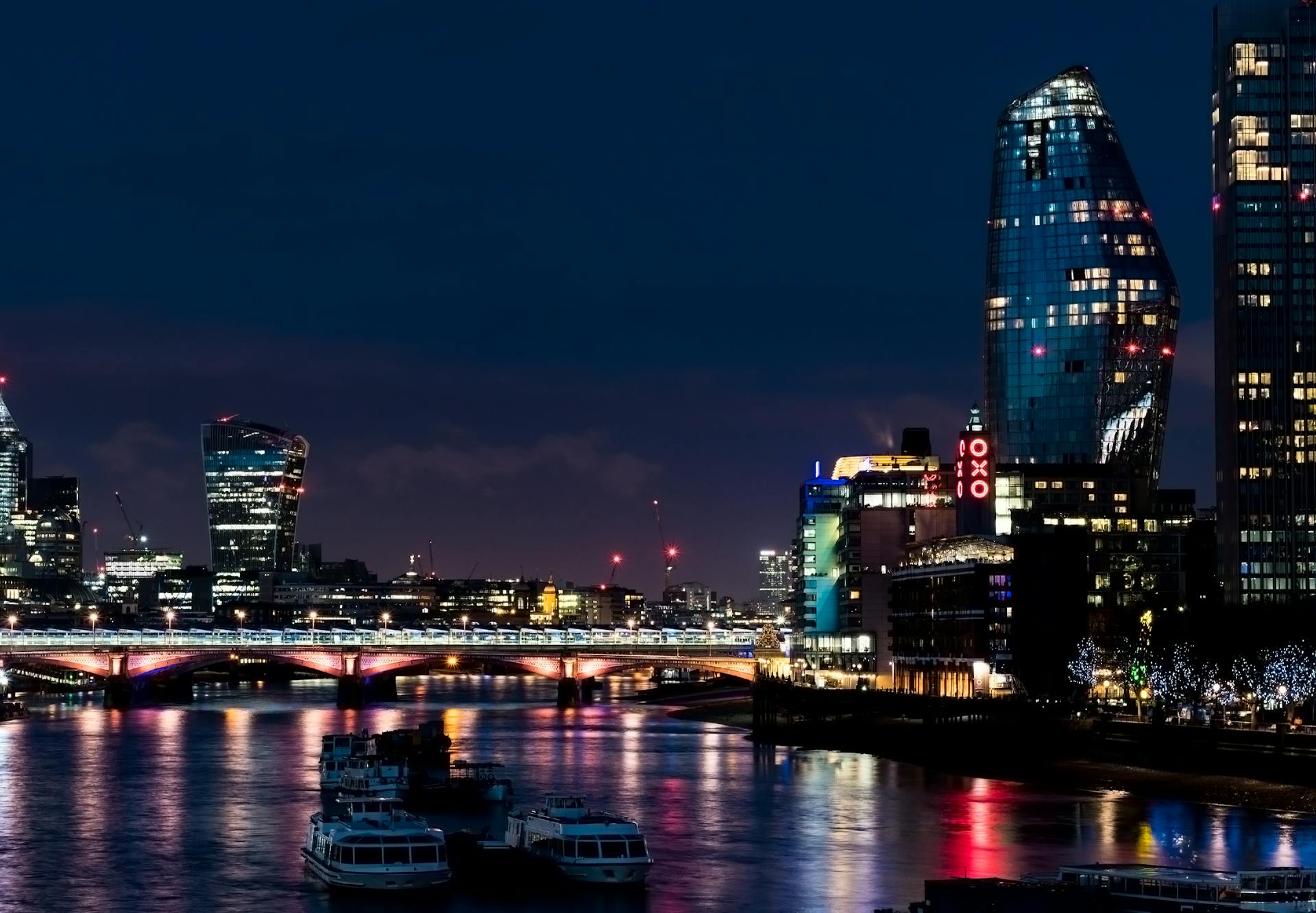 Stunning London cityscape at night featuring modern skyscrapers and bridges reflecting on the River Thames.