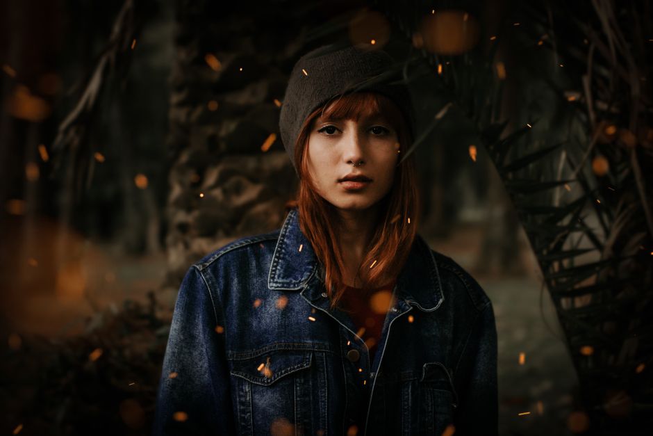 A serene young woman posing outdoors in a denim jacket, surrounded by warm autumn tones.