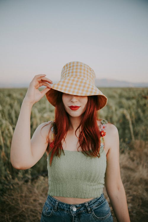 Young Woman in a Casual Outfit and a Bucket Hat Standing on a Grass Field 