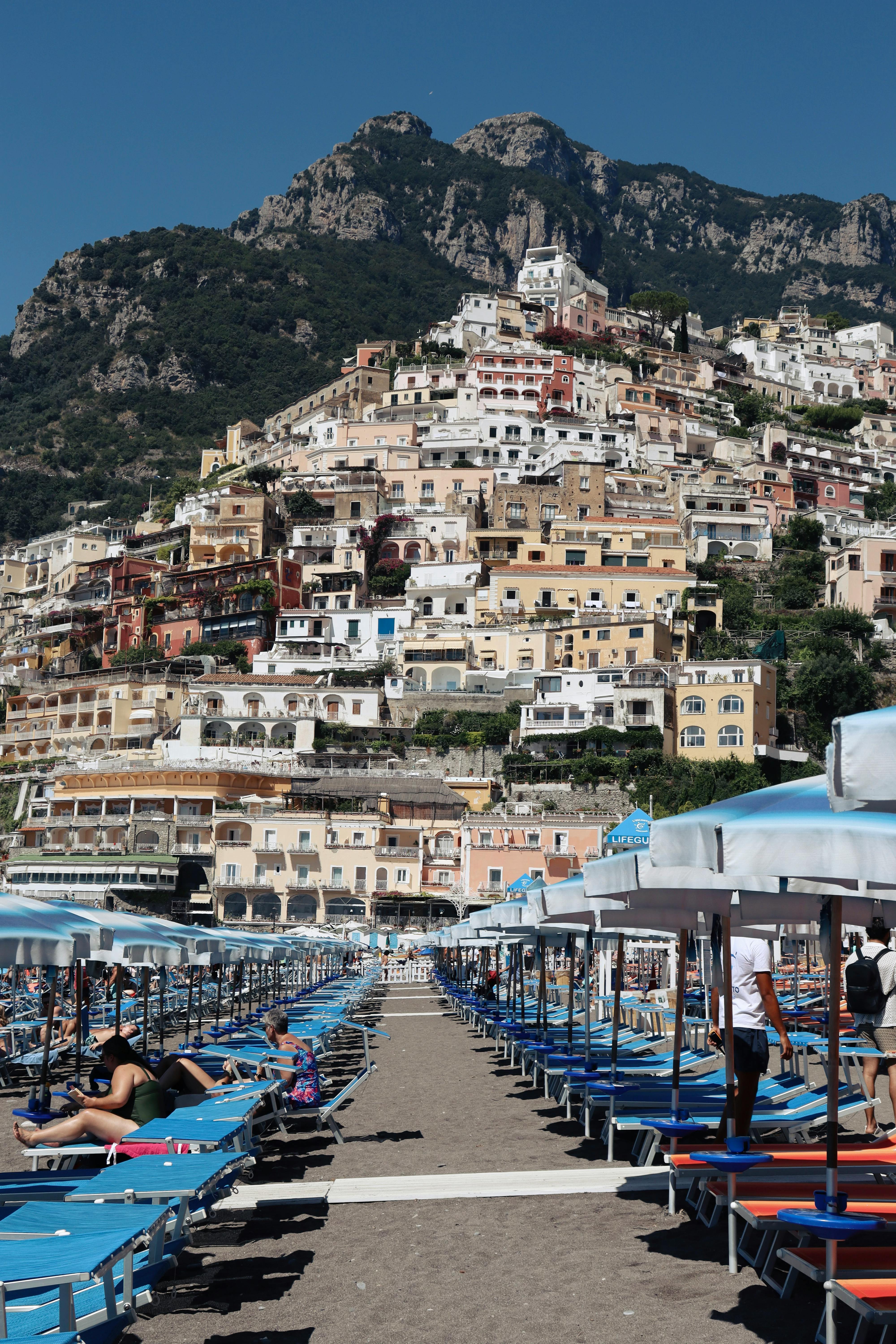 Experience the colorful cliffside homes of Positano, Italy, with a busy beach scene in the foreground.