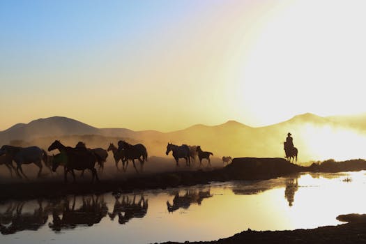 A herd of horses galloping by a river at sunset with a cowboy silhouette, creating a dramatic scene.