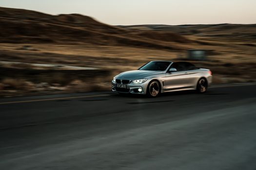 A sleek silver convertible car captures motion on a highway, showcasing luxury and speed.