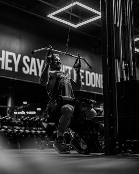 Muscular man performing a lat pulldown exercise in a modern gym, captured in a dramatic black and white style.