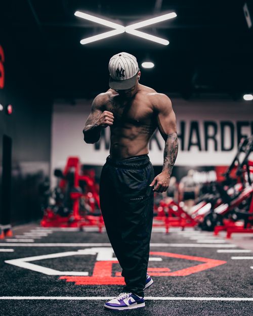 Free A shirtless muscular man wearing a cap, posing confidently in a gym with visible tattoos. Stock Photo