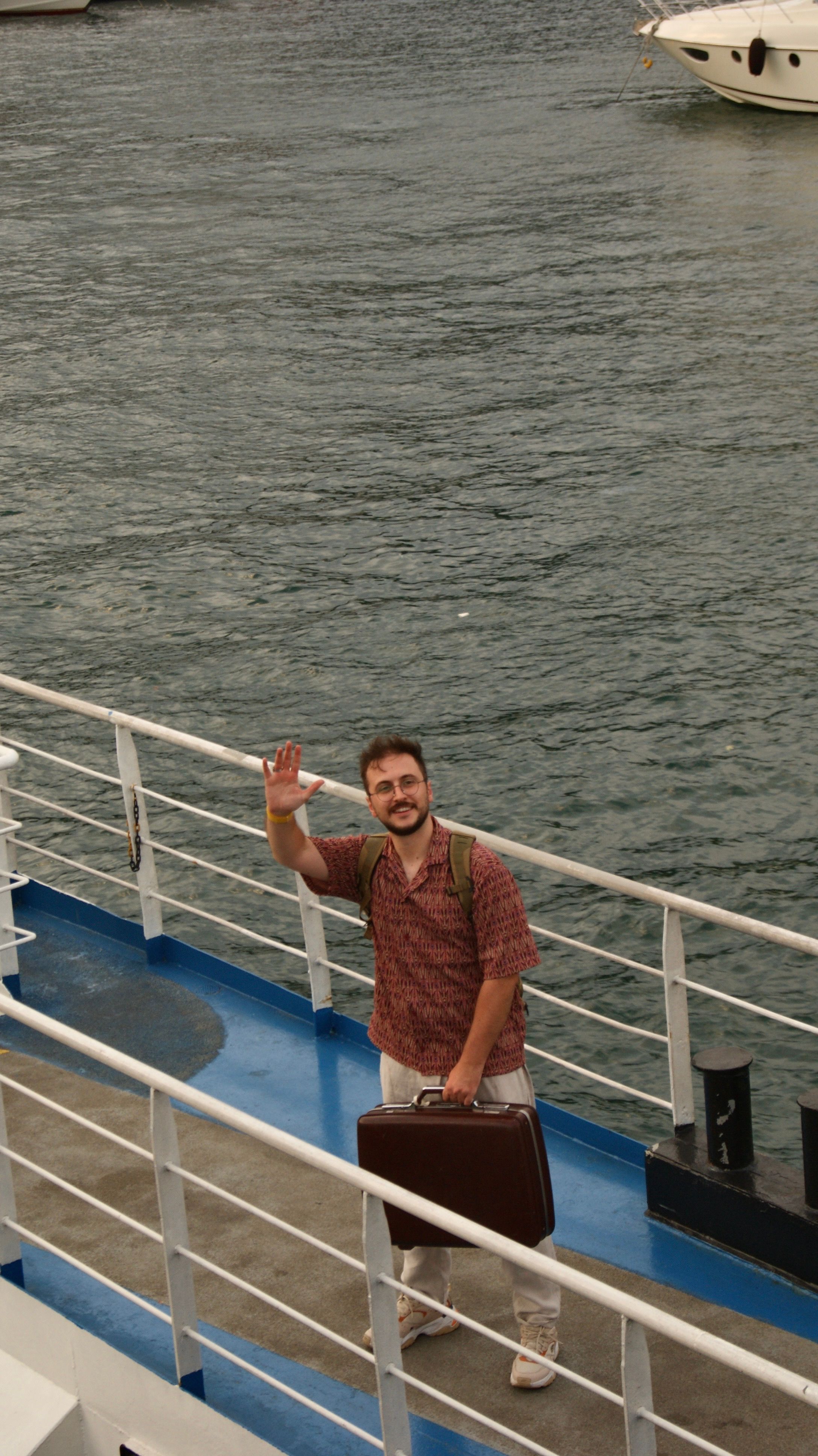 A man with a suitcase waves while boarding a boat at İstanbul harbor.