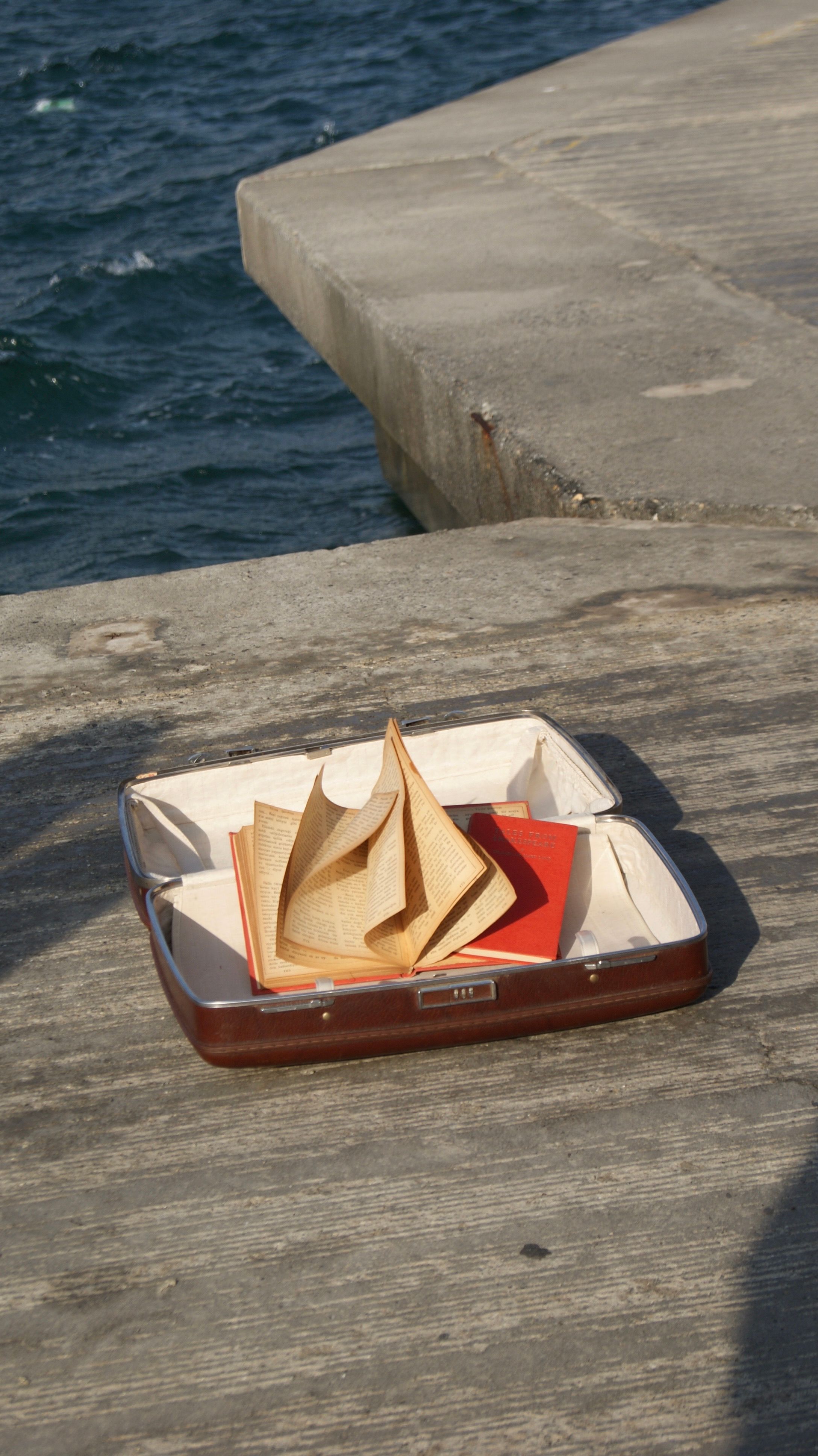 An open suitcase with a book on a wooden pier by the sea in Istanbul, Türkiye.