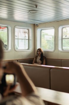 A woman sitting inside a ferry as a photographer captures her in the sunlight.