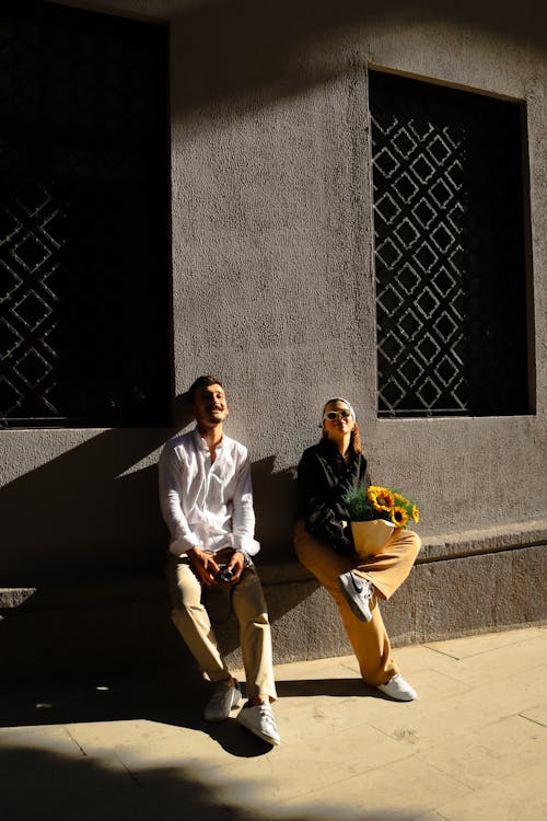 Woman and Man Sitting on Sunlit Wall
