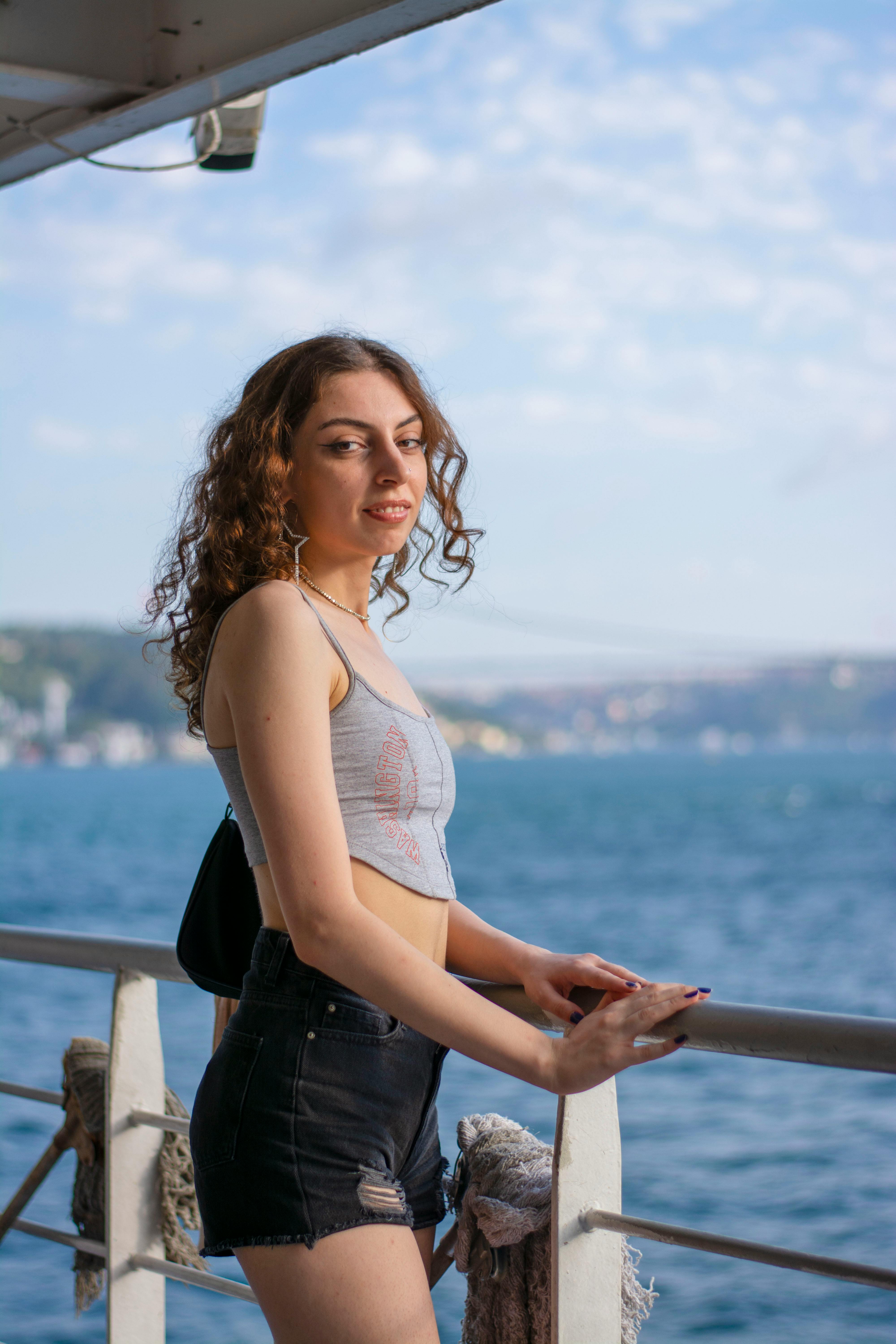 A young woman stands on a ferry, enjoying the view over a sunny summer sea.
