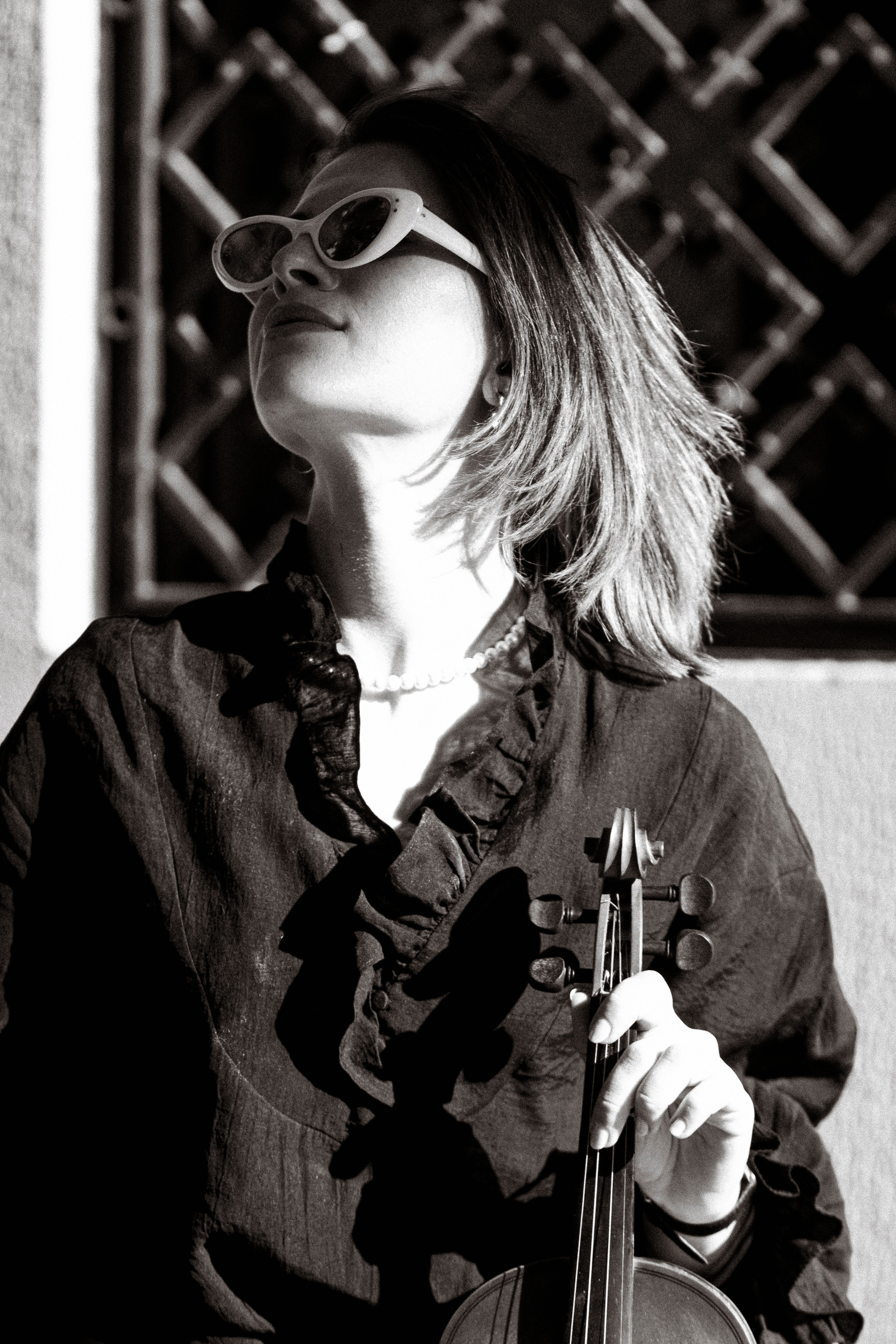 A black and white photo of a woman violinist in sunglasses holding a violin.