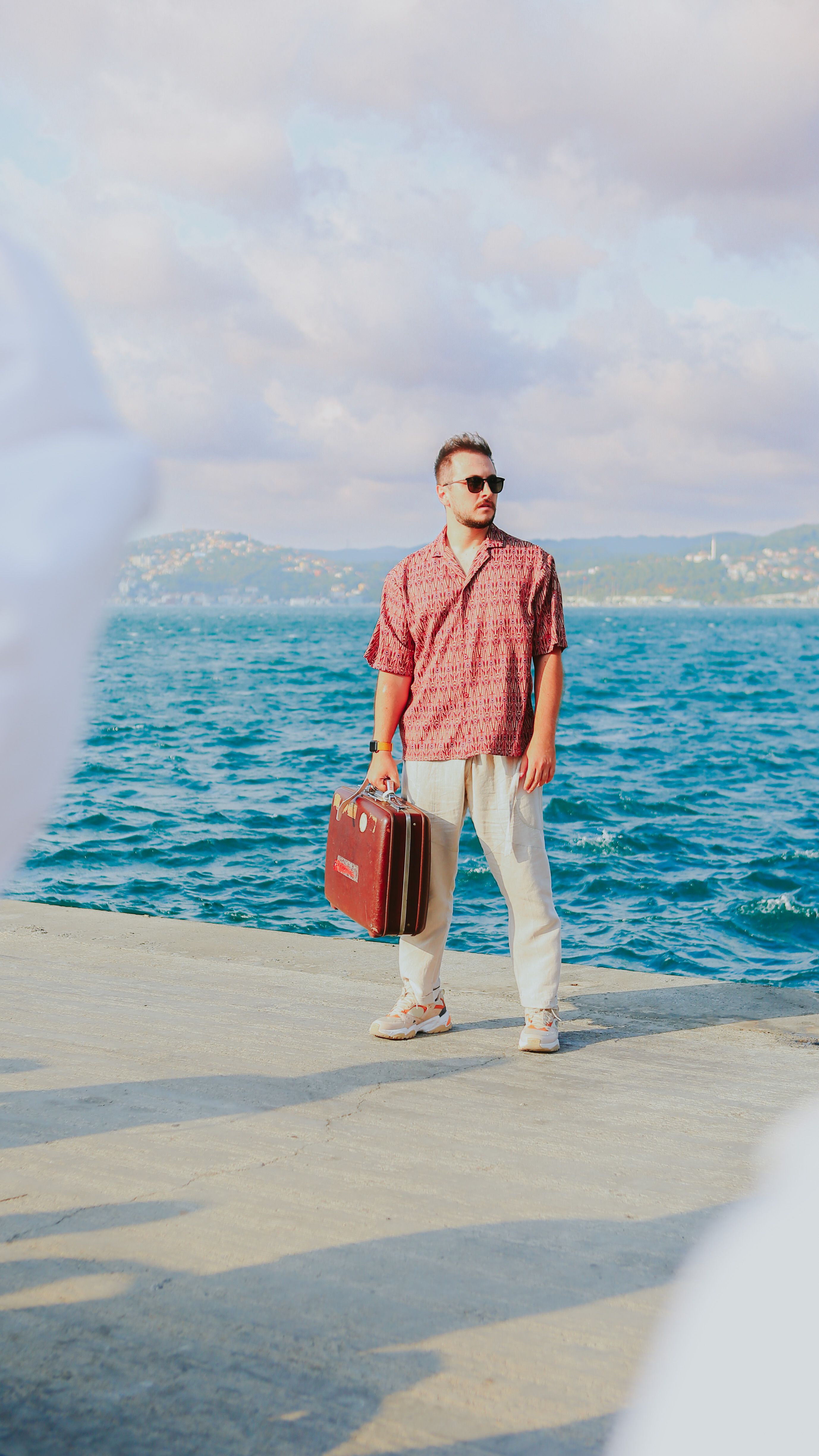 Casual man with vintage suitcase stands by the Bosphorus waterfront in Istanbul, enjoying summer travel.