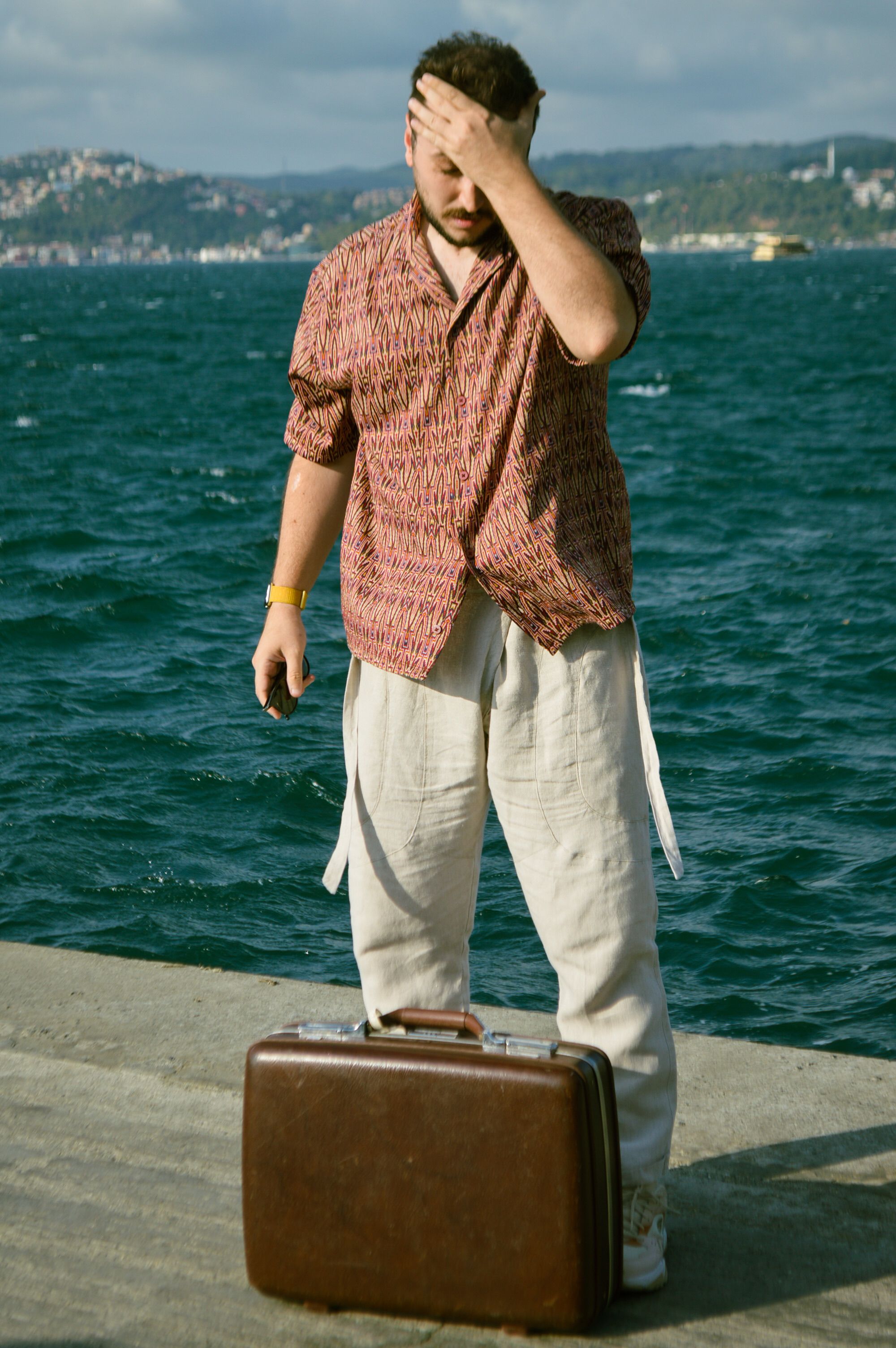 Man standing by the Istanbul seashore with a suitcase, showing a thoughtful expression.