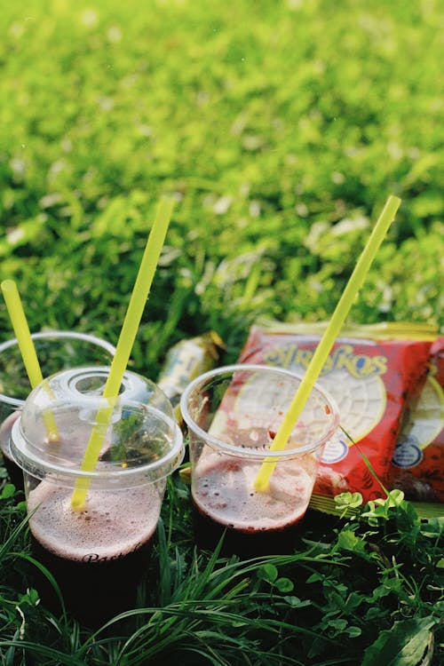 Drinks in Plastic Cups with Straws Standing on the Grass