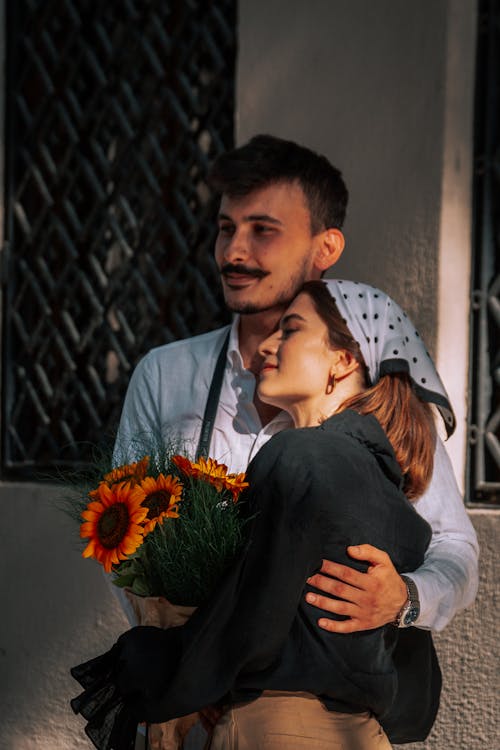 A Young Couple Hugging and Holding a Bouquet of Sunflowers 