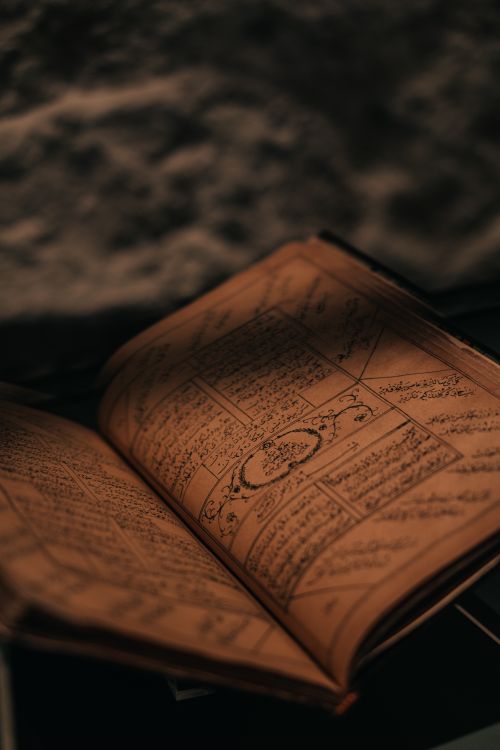 Free A close-up of a vintage open book displaying intricate Arabic calligraphy pages, evoking a retro and artistic feel. Stock Photo