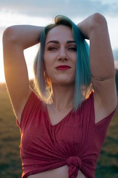Portrait of a stylish woman with blue hair posing confidently at sunset.