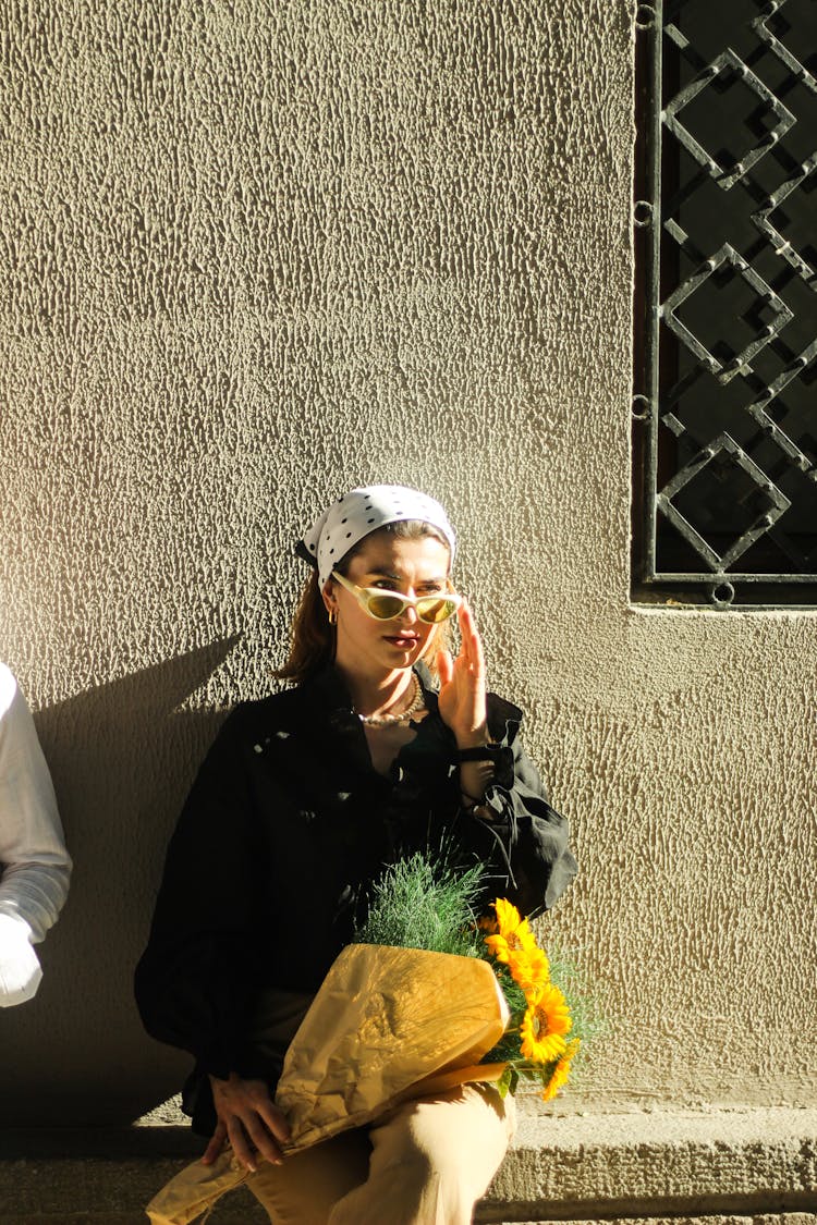 Woman In Black Blouse And Headscarf Sitting With Sunflower Bouquet