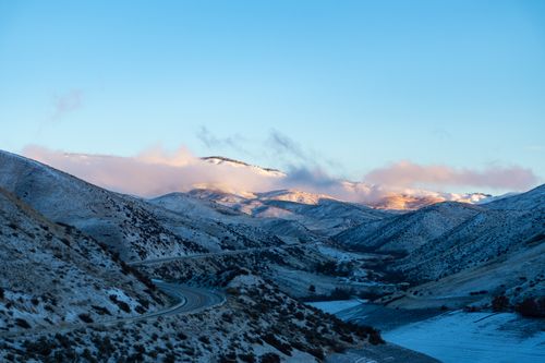 Free A breathtaking view of snow-capped mountains at sunrise with a winding road and a clear blue sky. Stock Photo