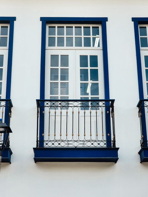 Free Stylish white building facade featuring modern balconies with blue trim and intricate railing design. Stock Photo