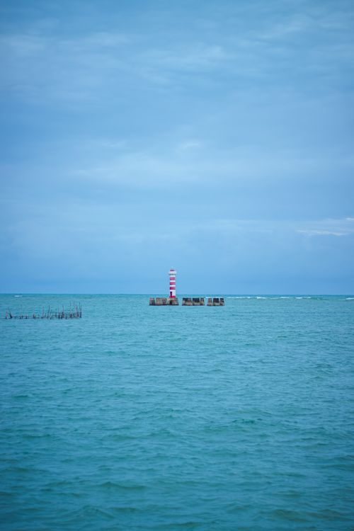 Free Elegant view of a distant lighthouse standing on a calm sea under a blue sky. Stock Photo