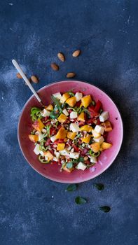 Fresh fruit and cheese salad in a pink bowl on a dark background with almonds.