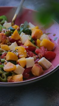 Fresh summer salad with peaches, tomatoes, and cheese in a pink bowl.