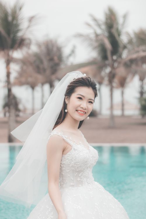 Free An elegant bride poses by the pool in a beautiful white wedding gown with a veil. Stock Photo