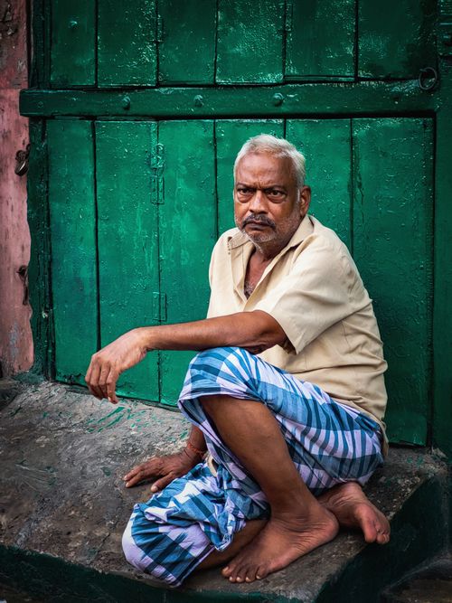 Free Senior man sitting barefoot outside a green door in Kolkata, India. Stock Photo