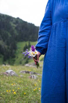 A woman holds a bouquet of wildflowers in a mountain meadow, showcasing tranquil nature.