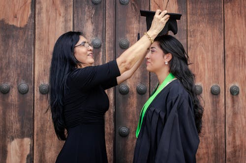 Woman Putting Academic Hat on Graduate Woman Head