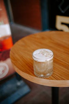 A creamy bubble tea with boba pearls in a short glass on a round wooden table, perfect for refreshing moments.