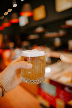 Aesthetic shot of a cold cocktail in a hand, capturing the vibrant atmosphere of a modern bar.