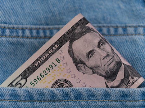 A five dollar bill tucked into a blue denim jeans pocket, symbolizing savings or cash on the go.