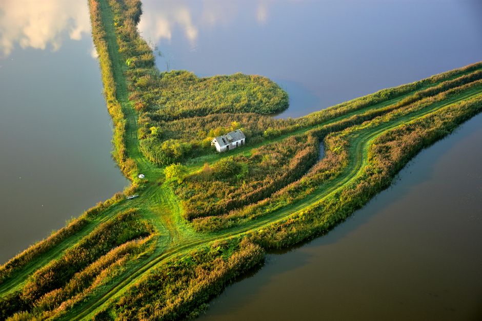 Drone shot of a lush green rural area with water and isolated building in Podlaskie, Poland.