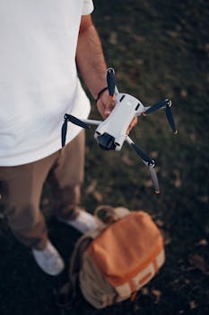Man holding a drone outdoors with a backpack on the ground, ready for adventure.
