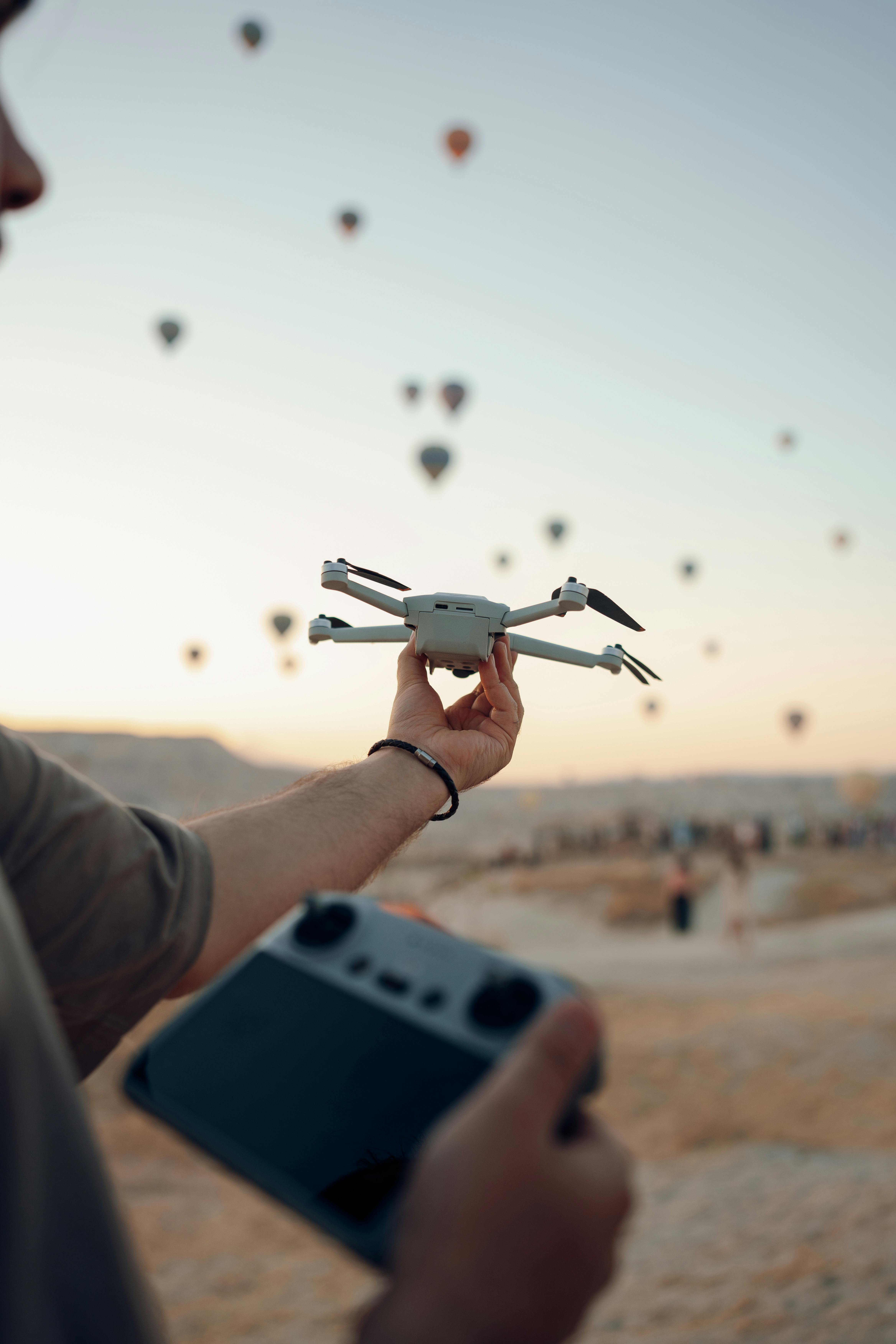 a man holding a drone and a controller on the background of flying hot air balloons