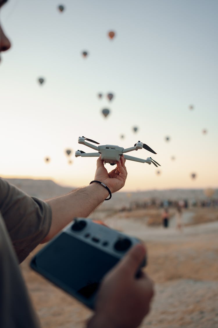 A Man Holding A Drone And A Controller On The Background Of Flying Hot Air Balloons 