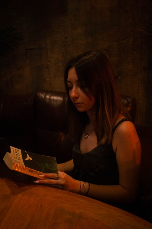 Free A young woman in a dark tank top is reading a book indoors with a warm glow. Stock Photo