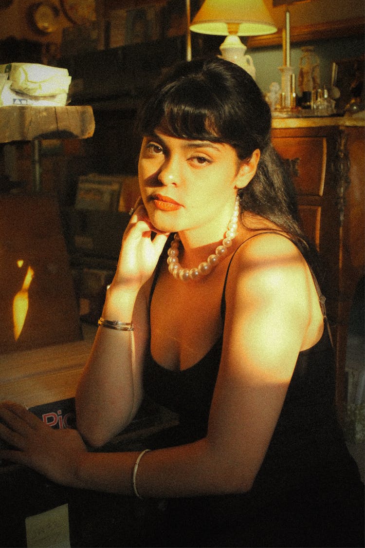 Woman In Black Tight Strap Dress And Pearls Holding Hand On Cheek