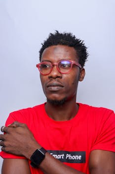 Man with red glasses and smartwatch posing against a white background in studio.