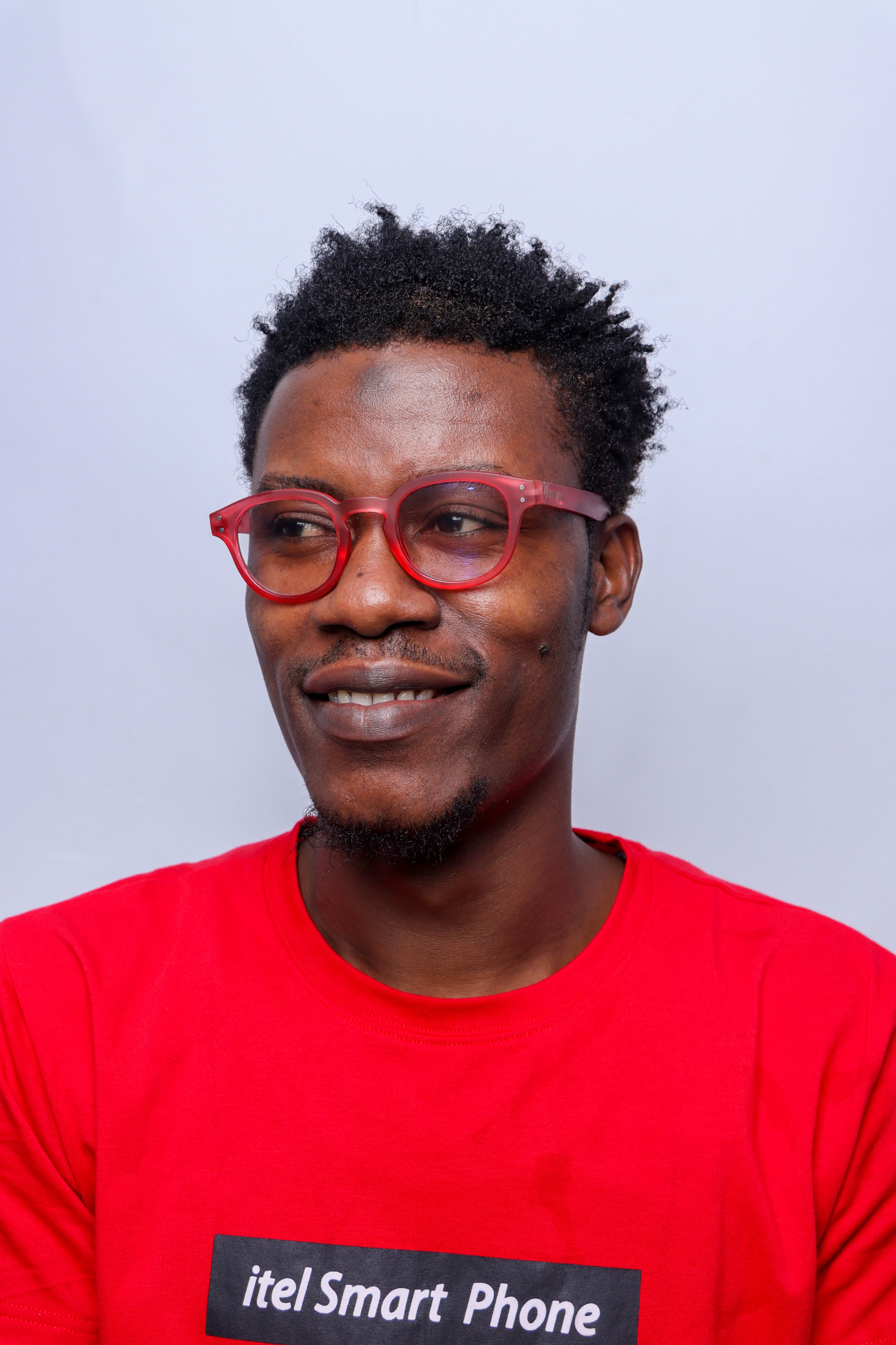 Studio portrait of an African man smiling, wearing red glasses and a red shirt.