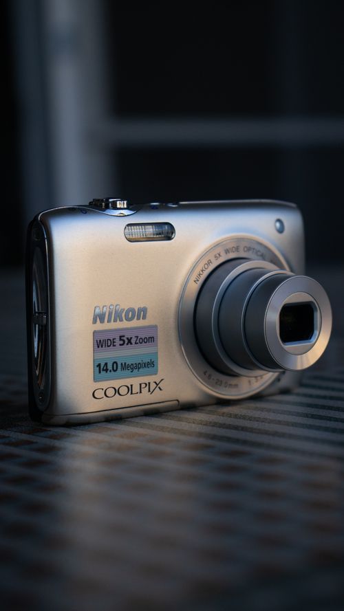 Free Close-up of a compact digital camera on a metallic surface, highlighting the lens and design. Stock Photo