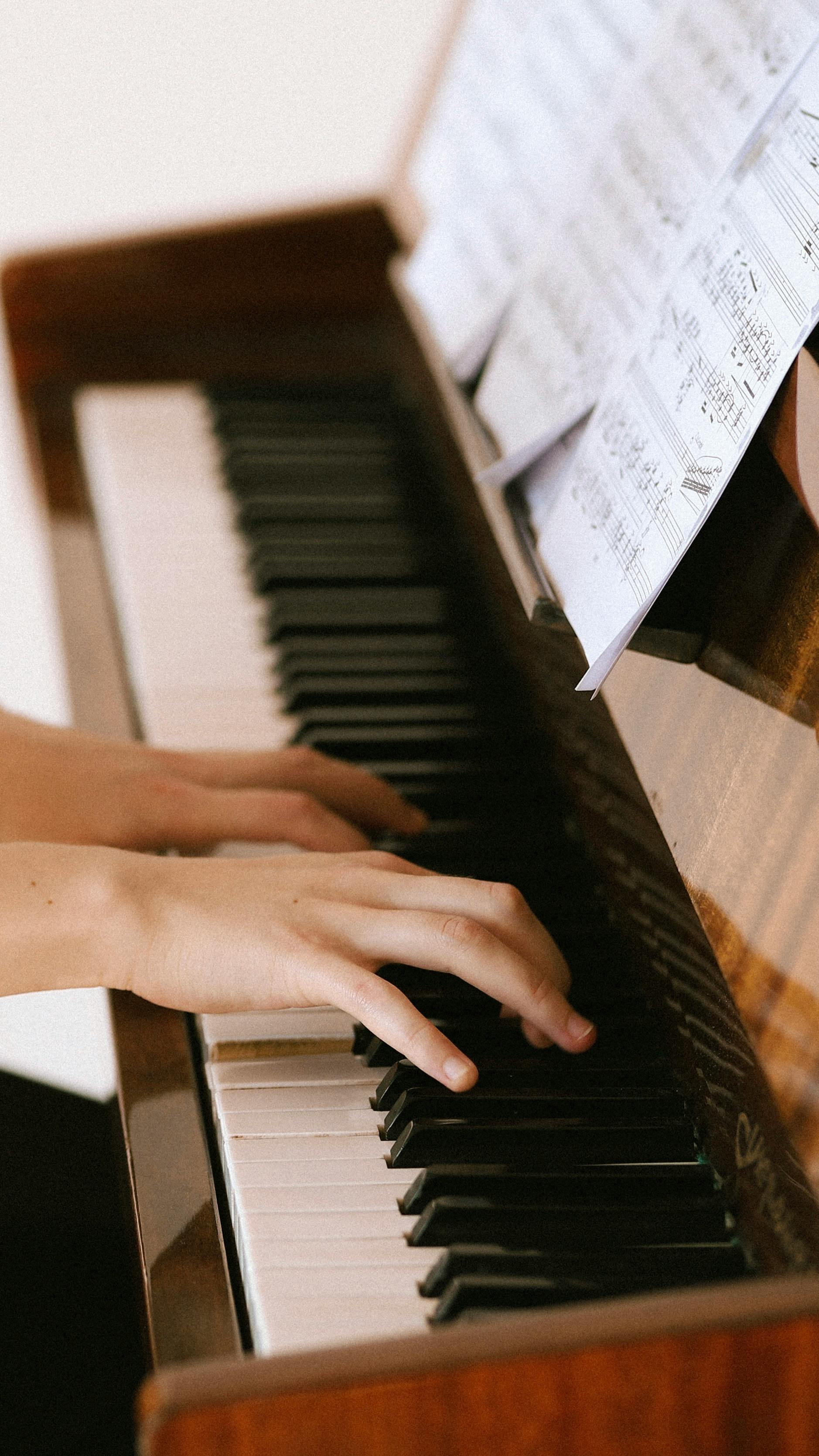 Close-up of hands playing piano keys with visible sheet music, creating a musical ambiance.